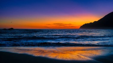 Akşamüstü Wairarapa 'daki White Rock plajında tek bir martı suyun üzerinde uçuyor.