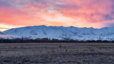Twizel yakınlarındaki karla kaplı sıradağların üzerinde canlı bir günbatımı.