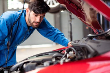 Otomobil tamircisi genç adam otomotiv radyatörü kaputunu otomobil tamirhanesinde kontrol ediyor ve onarıyor. Araç bakım konseptinden sonra çalışan motor teknisyeni.