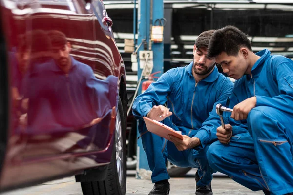 automotive mechanic men checking at car tyre rubber condition needed for replacement, man pointing hand at wheel following maintenance checklist document, after service at auto repair shop concept