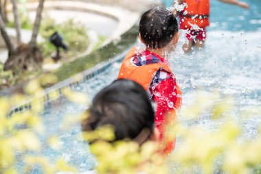 Asyalı çocuk can yeleği giyiyor yazın yüzme havuzunda su oynuyor.