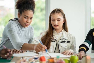 Group of diversity students enjoy drawing and painting in arts class with friends. happy smiling kids using paintbrush sketching on paper. support creative skill in a classroom at school. 