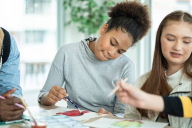 Group of diversity students enjoy drawing and painting in arts class with friends. happy smiling kids using paintbrush sketching on paper. support creative skill in a classroom at school. 