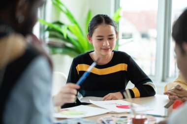 Group of students enjoy drawing and painting in arts class with friends. happy smiling kids using paintbrush sketching on paper. support creative skill in a classroom at school. 
