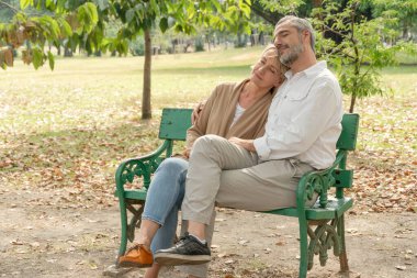 Happy senior couple embrace together and relax resting on bench at park in summer nice weather. love marriage life goal. healthy lifestyle retirement people concept