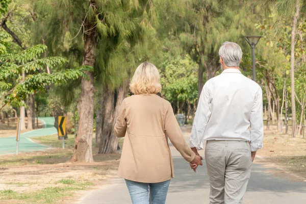 Back of man and woman holding hand and walking at park, Love marriage lifestyle goals, Happy retirement elder couple spending time, talking, sharing and relaxing together, life insurance concept