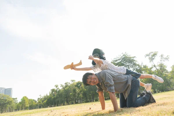 Asian boy wearing pilot helmet playing airplane toy on father back at park. dad support kid dream goal or aspiration. life living and family insurance concept. copy space