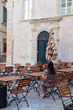 Kadın turist Dubrovnik şehrinin antik sokaklarındaki boş bir sokak kafesinde bir masada oturuyor. Hırvatistan. Avrupa. Ünlü turizm merkezi, turizm beldesi