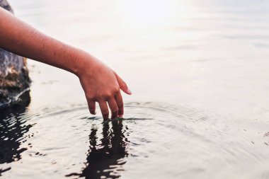 İnsanın eli doğanın ortasında suya dokunuyor.