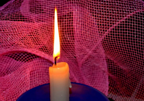 Close-up of female hands lighting a candle with a match in the dark, it burns against a pink grid and after a while a gust of wind extinguishes it.
