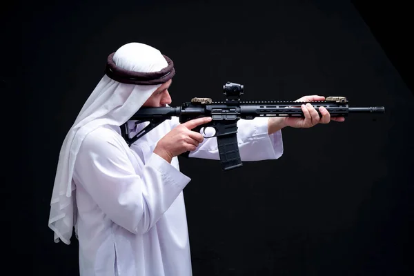 伝統的なドレスのアラブ人を撃つ準備ができて黒の背景に隔離された手にライフルを保持します 銃を持つ武装したイスラム教徒の男は 伝統的なドレスやスカーフを着ていた 神戸市の中東人 — ストック写真