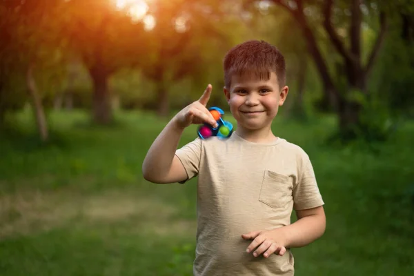Funny Smiling Boy Playing with Spinner in a Sunny Day in the Park. 6 Years Old Guy Has a Spinner in his Hand. Outdoor with Son. High quality photo
