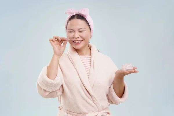 Asian Woman Wearing Bathrobe Smiling While Smelling Cosmetic Cream Toned — Stock Photo, Image