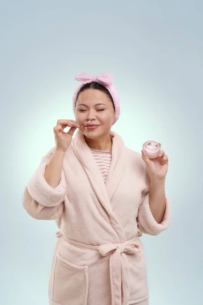 Senior Asian Woman Bathrobe Smelling Cosmetic Cream While Standing Blue — Stock Photo, Image