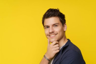 Yakın plan portrede eli çenesine yakın gülümseyen, yakışıklı genç bir adam var. Kendine güveni, cazibesi ve çekiciliği var. Yüksek kalite fotoğraf