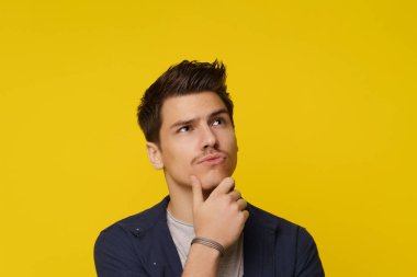 Close up of young man on yellow background, with facial expression conveying confusion and uncertainty, as he thinks and has doubt. Complex and emotional nature of decision-making and contemplation clipart