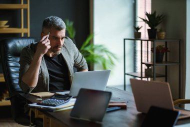 Takım elbiseli orta yaşlı yakışıklı işadamı, dinamik kurumsal ortamda hırs ve kararlılık sergileyerek, çatı katında özveri ve profesyonellik gösteriyor. Yüksek kalite