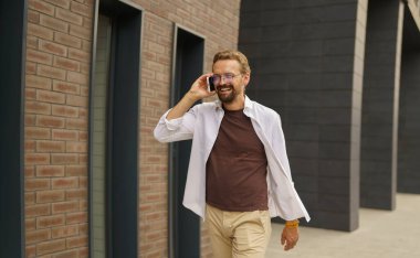 Cep telefonuyla konuşurken sokakta yürüyen mutlu bir adam. Yüzünde parlak bir gülümseme, neşe ve pozitiflik hissi yayar. - Evet. Yüksek kalite fotoğraf