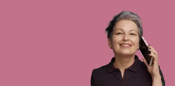 stock image Successful Mature Woman Engages In Conversation On Mobile Phone, Isolated Against Pink Background. Concept Of Communication In Old Age, Showcasing Positive And Confident Use Of Technology By Seniors