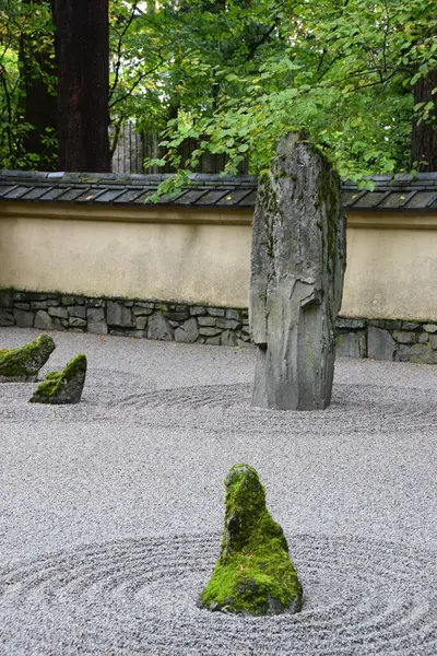 Portland Oregon 'daki Japon bahçesindeki uzun bir kayayı işaret eden üç yosunlu taş. Taşların etrafındaki çakıllar sudaki dalgalar gibi kuru bir zen bahçesi.