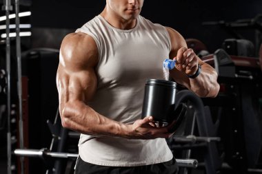 Kaslı bir adam konteynır tutuyor. İçinde beslenme, protein ve süt var. Spor beslenmesi