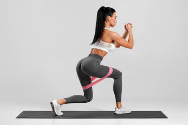 Gri arka planda direnç bandıyla kalça kasları için egzersiz yapan atletik kız. Spor salonundaki kadın.