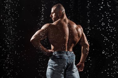 Muscular man under the rain in studio. Sexy male in water drops