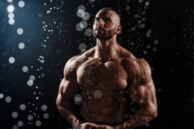 Stüdyoda yağmur altında kaslı bir adam. Su damlaları içindeki seksi erkek, karın kası.
