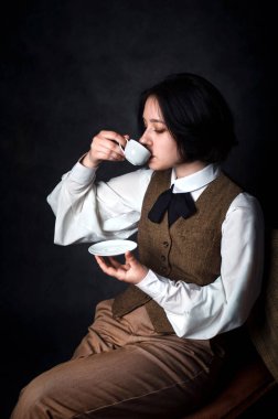 Klasik erkek giyimli, çay fincanından içen genç bir kadın dedektifin stüdyo portresi Sherlock Holmes 'un zamansız görüntüsünü incelikli ve incelikli bir şekilde referans veriyor..