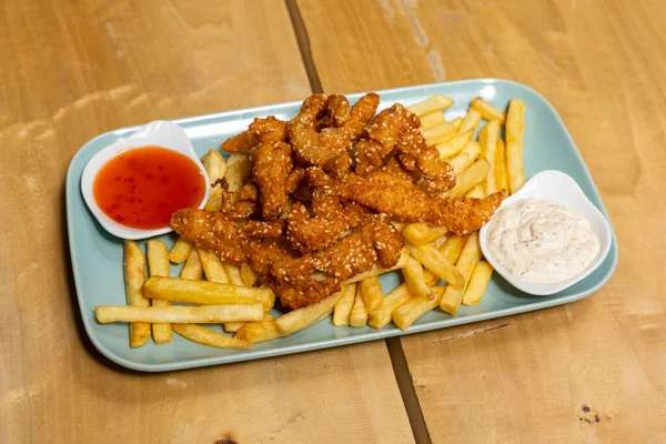 Sesame chicken fingers served on a wooden board with french fries and dipping