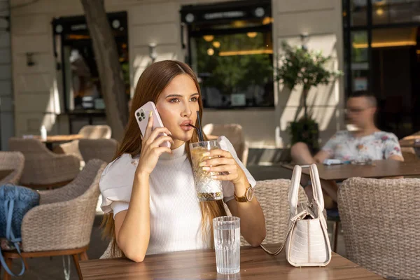 Young woman drinking coffee alone talking on her smartphone