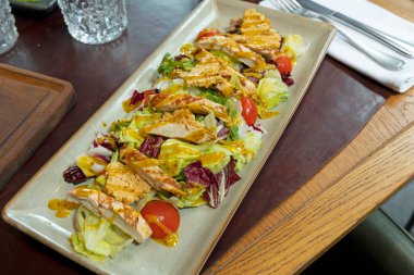 Chicken stripes on crispy lettuce with cherry tomatoes, bacon and goat cheese chips