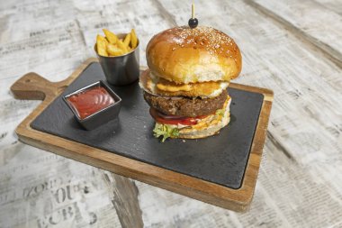 Beef burger served on a board with french fries in the restaurant