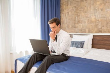 Hüsrana uğramış iş adamı otel yatağında oturmuş elini başının üstünde tutuyor.