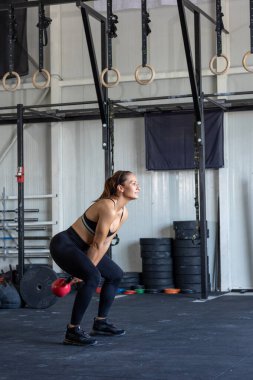 Spor salonunda kettlebell egzersizi yapan bir kadın.