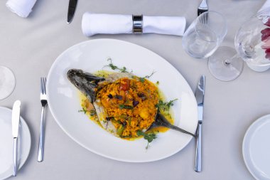 Beyaz tabakta pilavla servis edilen levrek.