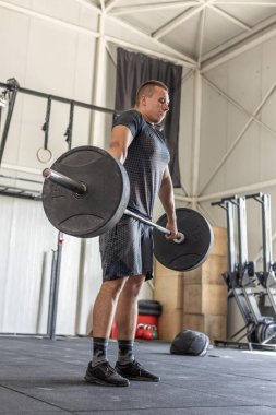 Endüstriyel spor salonunda halteri kaldıran adam.