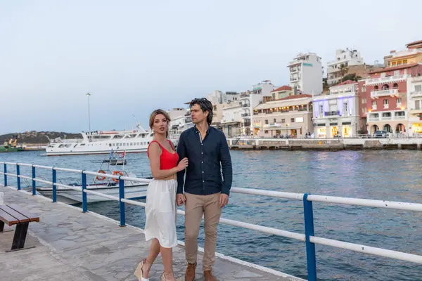 Deniz kenarında yürüyen çift, arka planda Avrupa tarzı renkli binalarla sarılıyorlar.