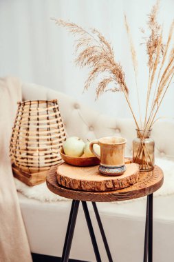 Cozycore ya da cottagecore konsepti, sıcak kahverengi bej iç tasarım nesneleri. Kanepede rahat yün ekose, tahta fenerde yanan mum, ahşap masada çay fincanı. Sıcak renk fotoğraf düzenleme.