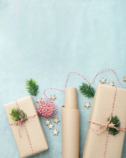 自然茶色の包装紙とギフト包装袋クラフト紙または袋紙と呼ばれる 赤と白の紙の文字列で飾られた贈り物 青い背景に小さな木の星とモミの木の枝 — ストック写真