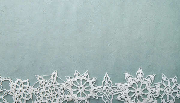 Christmas or winter products background, blue rough crafts paper lower edge decorated with handmade crochet snowflakes, lot of copy space.
