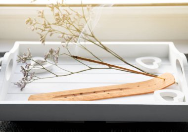 Scent Styling konsepti. Beyaz tepside yanan tütsü mumu ile ev penceresi pervazı, güzel kokulu iyi bir ruh hali yaratır..