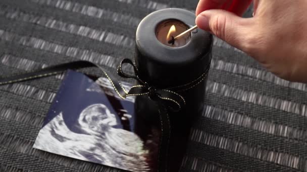 妊娠損失または悲しみカウンセリングの概念的なイメージ 赤ちゃんの超音波画像黒のリボン燃焼と黒のキャンドルの横にある — ストック動画