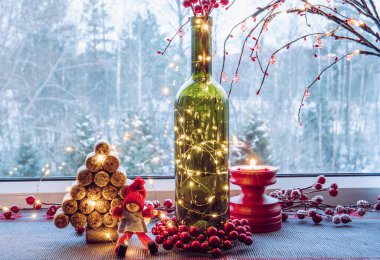 Şarap şişesiyle doldurulmuş Noel süslemeleri mikro ışıklarla dolu ve kullanılmış şarap mantarlarıyla yapılmış ladin ağaçları, sevimli klasik elf heykelcikleri, arkasında karlı kırsal orman pencereleri var.. 