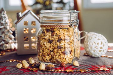 Ev yapımı Noel hediyesi kavramı, çeşitli fındıklı ve güzel cam kavanozda kuru üzümlü el yapımı granola. Bulanık Noel ağacı ve arka planda ışıklar.
