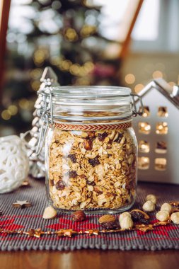 Ev yapımı Noel hediyesi kavramı, çeşitli fındıklı ve güzel cam kavanozda kuru üzümlü el yapımı granola. Bulanık Noel ağacı ve arka planda ışıklar.