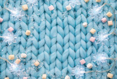 Açık mavi yumuşak örgü desenli arka plan, kar tanesi şeklindeki ip ışıkları, sahte kar ve mini marşmelovlar, kopyalanmış noel aralığı..