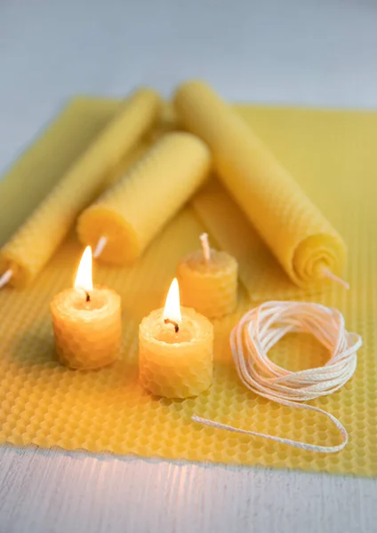 Natural rolled beeswax candles from pressed beeswax honeycomb sheet at home indoors. Hobby concept. Two candles lit and burning.