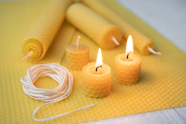 Natural rolled beeswax candles from pressed beeswax honeycomb sheet at home indoors. Hobby concept. Two candles lit and burning.