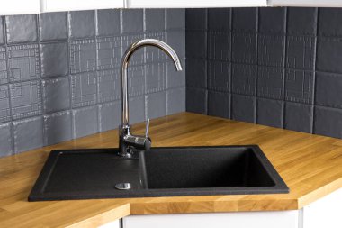 Yeni, modern mutfak, ahşap kasap, siyah dikdörtgen granit lavabo ve gri renkli kiremit duvarla kaplı meşe tezgahının yakın görüntüsü. Köşedeki dolap..